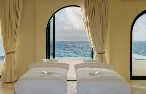 a room with four white beds in front of a window at Cap Juluca, A Belmond Hotel, Anguilla in West End Village