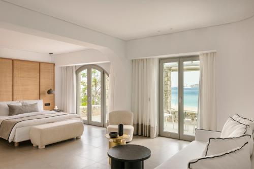 a white bedroom with a bed and a couch and chairs at Grace Mykonos in Agios Stefanos