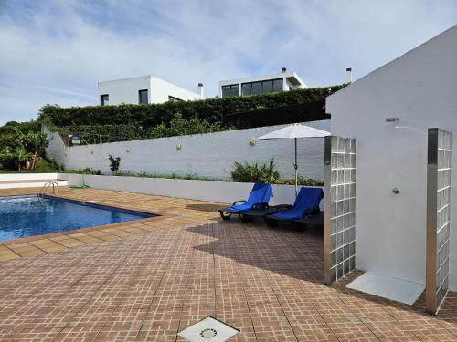 a patio with two chairs and an umbrella next to a pool at Casa dos Amigos in Ponta Delgada