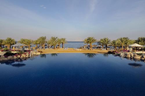 a view of a beach with palm trees and a swimming pool at Mövenpick Resort & Spa Tala Bay Aqaba in Aqaba