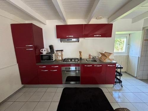 La cuisine est équipée de placards rouges et d'un four avec plaques de cuisson. dans l'établissement Petite maison à la campagne, à Mespaul