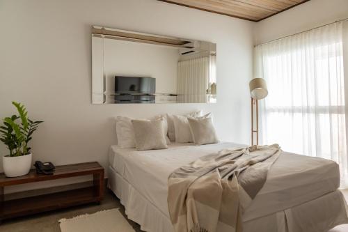a white bedroom with a bed and a mirror at Hotel Boutique Frangipani in Brotas