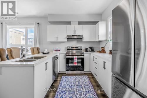 La cuisine est équipée de placards blancs et d'un réfrigérateur en acier inoxydable. dans l'établissement Cozy 3 story Townhouse!, à Niagara Falls