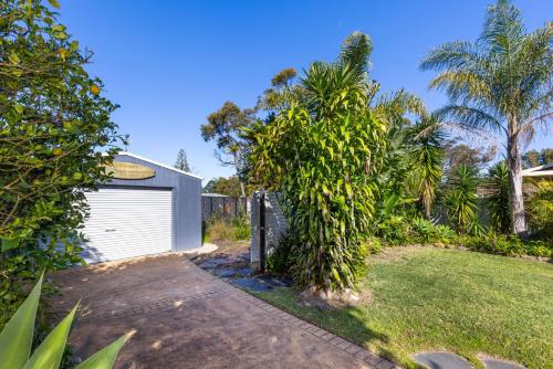a garage with a tree next to a yard at The Anchor - Pet Friendly - 5 Mins Walk to Beach - EV Charging in Callala Beach