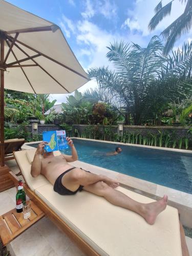 a woman laying on a bench reading a book next to a swimming pool at Bali Village Villa in Perean
