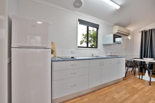 a kitchen with white cabinets and a sink and a table at Tasman Holiday Parks - Fisherman's Beach in Emu Park