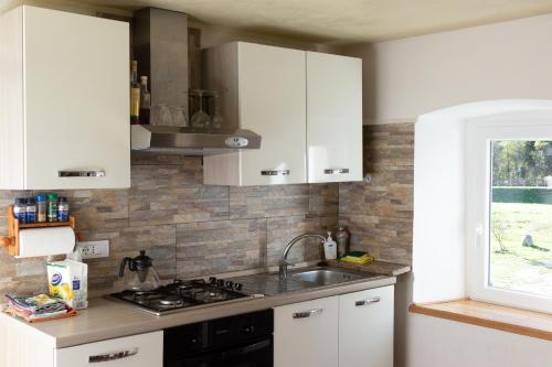 eine Küche mit weißen Schränken, einem Waschbecken und einem Fenster in der Unterkunft Valdastico Casetta in sasso con giardino in Pedemonte