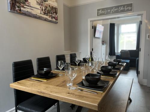 a long wooden table with chairs and wine glasses at Spacious home sleeps 8 Nr Etihad Coop Live & City in Manchester