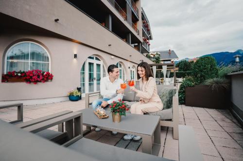 a man and woman sitting on a balcony drinking wine at Hotel Bellavista in Cavalese