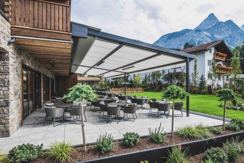 a patio with tables and chairs with mountains in the background at Bergresort Zugspitze Ehrwald by ALPS RESORTS in Ehrwald