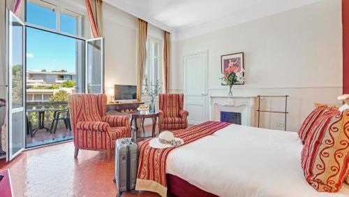 サント・マキシムにあるHotel Les Tourellesのベッドルーム1室(ベッド1台、椅子2脚、暖炉付)