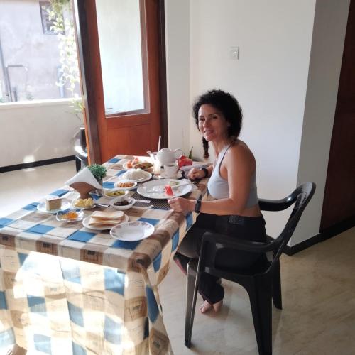 Eine Frau, die an einem Tisch mit Teller Essen sitzt. in der Unterkunft R & R Home Stay in Negombo