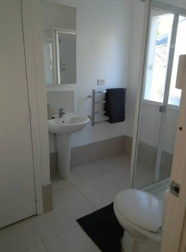 a white bathroom with a toilet and a sink at Ahu in Piha