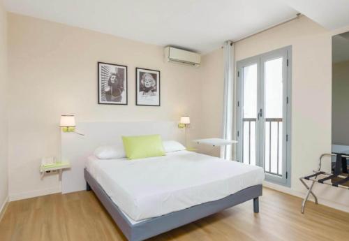 a white bedroom with a bed and a large window at B&B HOTEL Antibes Juan-les-Pins in Juan-les-Pins