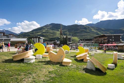 un groupe de bancs dans un champ avec des montagnes en arrière-plan dans l'établissement Belambra Clubs Résidence Les Menuires - Le Hameau Des Airelles, aux Menuires