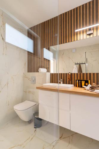 a white bathroom with a toilet and a sink at Olivina Park Spa - domki z dostępem do krytego basenu, saun, wyżywienia i atrakcji dla dzieci in Niechorze