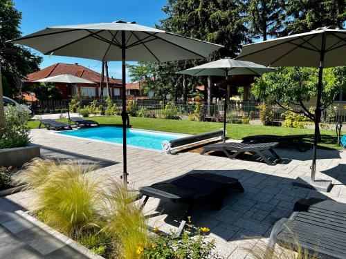 a pool with two umbrellas and two chairs and a table and benches at Best Apartman Boglár in Balatonboglár