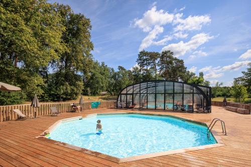 a person standing in a swimming pool next to a glass house at Huttopia De Meinweg in Herkenbosch