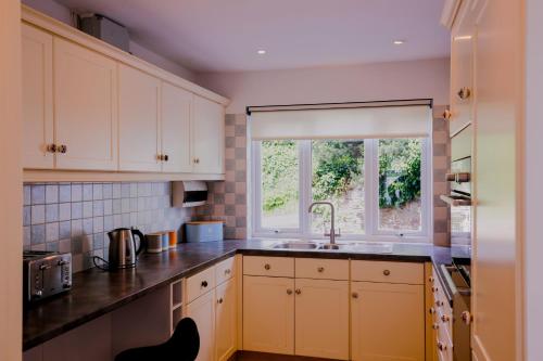 a kitchen with white cabinets and a sink and a window at St Anthony Cottage in Saint Mawes