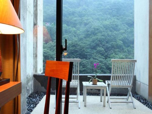 balcón con 2 sillas, mesa y ventana en Volando Urai Spring Spa & Resort en Wulai