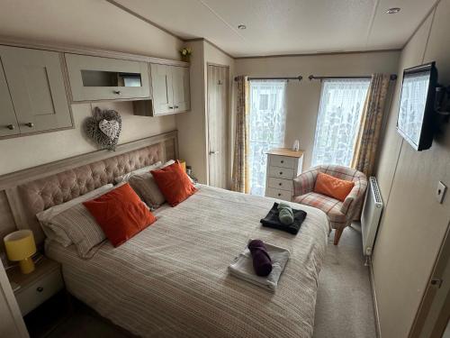 Luxury Lake District Holiday Home-Sleeps 4 في كوكيرماوث: غرفة نوم مع سرير مع وسائد برتقالية وكرسي