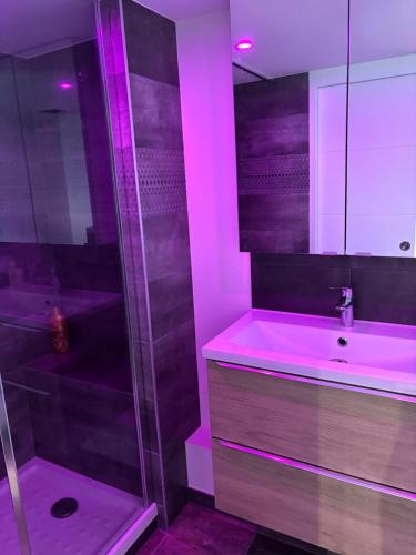 La salle de bains est pourvue d'un lavabo et d'une douche avec un éclairage violet. dans l'établissement Sweet home Kaysersberg, à Kaysersberg