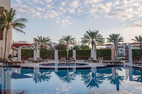 - une piscine bordée de chaises et de palmiers dans l'établissement Wateera Jebel Sifah, à As Sīfah