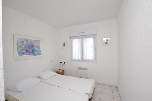 Cette chambre blanche dispose de deux lits et d'une fenêtre. dans l'établissement Le Baroncelli sur la plage, au Grau-du-Roi