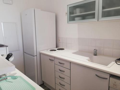 La cuisine blanche est équipée d'un évier et d'un réfrigérateur. dans l'établissement Bas de villa, vue mer, terrasse, clim, piscine, à Toulon