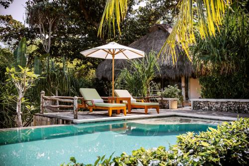 a swimming pool with two chairs and an umbrella at NIHI Sumba - 50 Best Hotels of the World in Watukarere