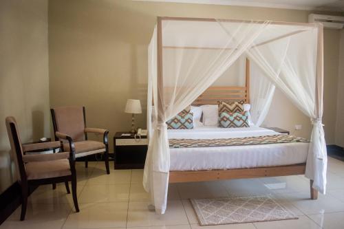 ein Schlafzimmer mit einem Himmelbett und einem Stuhl in der Unterkunft Lotus by Serendib in Blantyre