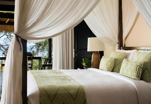 a bedroom with a large bed with curtains and a window at NIHI Sumba - 50 Best Hotels of the World in Watukarere