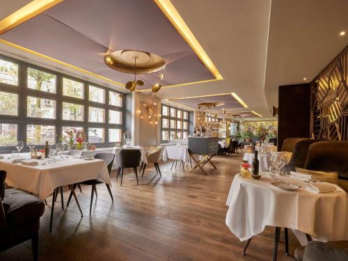 un restaurante con mesas y sillas blancas y ventanas en Sofitel Legend The Grand Amsterdam en Ámsterdam