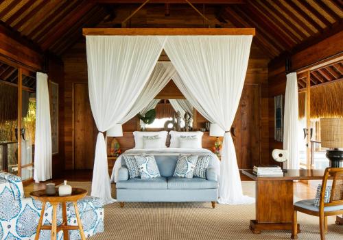 a bedroom with a canopy bed with a blue couch at NIHI Sumba - 50 Best Hotels of the World in Watukarere