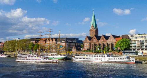 een groep boten aangemeerd in een rivier met een kerk bij Best Western Hotel Bremen City in Bremen