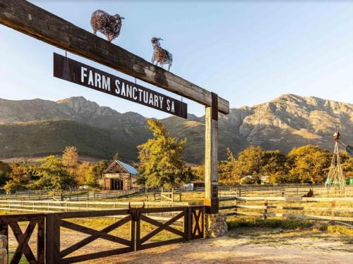 a sign for a farm with mountains in the background at Extraordinary Barn Loft at Animal Sanctuary in Franschhoek