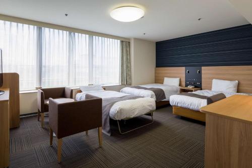a hotel room with three beds and a table at Comfort Hotel Hakata in Fukuoka