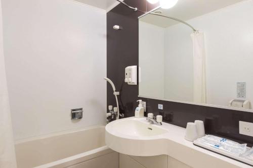 Baño blanco con lavabo y espejo en Comfort Hotel Naha Prefectural Office en Naha