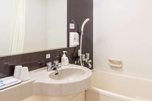 een badkamer met een wastafel, een spiegel en een bad bij Comfort Hotel Kokura in Kitakyushu