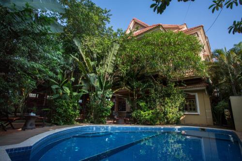 a swimming pool in front of a house with trees at Le Tigre Hotel in Siem Reap