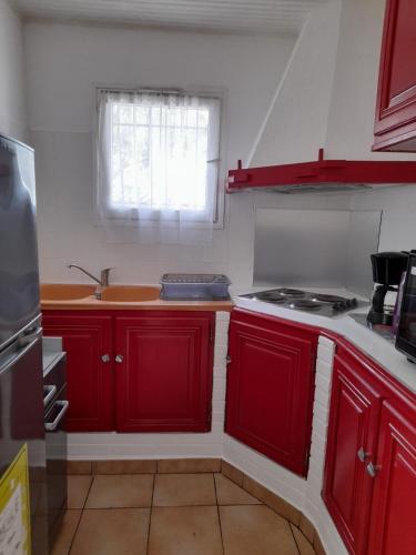 d'une cuisine avec des placards rouges, une cuisinière et une fenêtre. dans l'établissement Charmant appartement de vacances, à Argelès-sur-Mer