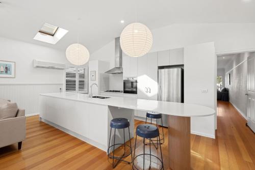 a kitchen with a large white counter and stools at Swyn Y Mor Riverside Cottage Haven in Ocean Grove