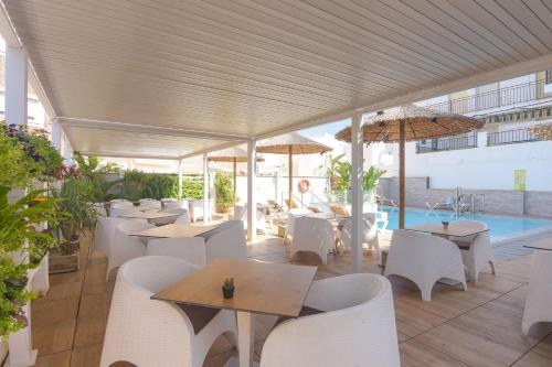 un restaurante con mesas y sillas blancas y una piscina en Hostal La Ermita, en Nerja