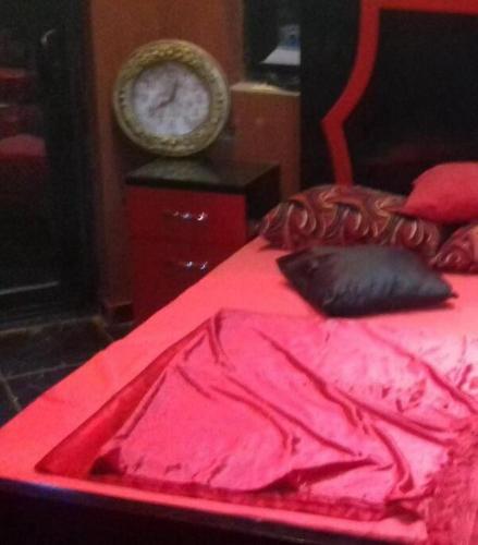 a red bed with a red blanket and a clock at Villa Mostafa Sadek, Swimming pool, Tennis & Squash - Borg ElArab Airport Alexandria in Borg El Arab