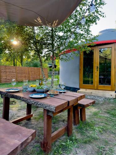 a wooden picnic table in a yard with wine glasses at Jurta nad Zegrzem z prywatnym jacuzzi in Arciechow