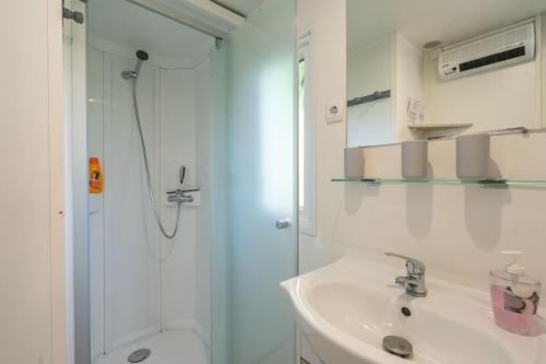 Un baño blanco con ducha y lavabo. en Mobil home La Palmyre 4etoiles, en Les Mathes