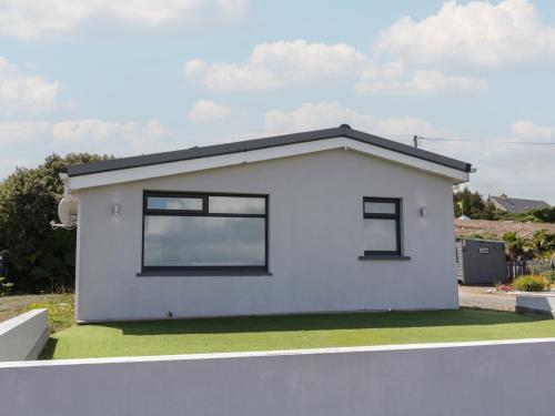 a white house with black windows on a green lawn at Tory Island View in Mín Lárach