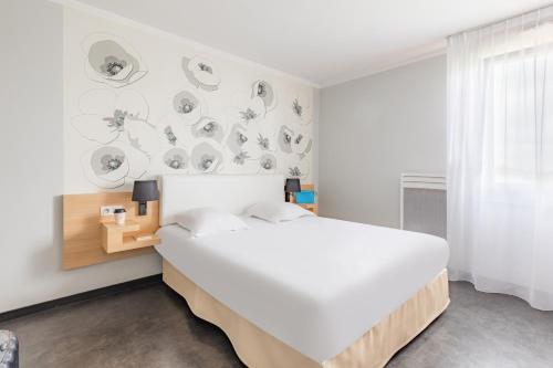 a white bedroom with a large bed and a wall with plates at Appart'City Classic Reims Parc des Expositions in Reims