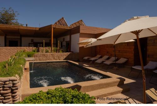 een zwembad met een parasol en stoelen en een huis bij Terrantai Lodge in San Pedro de Atacama