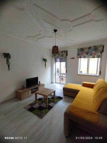 a living room with a yellow bed and a table at Apartamentos das Avós-Flor in Nazaré